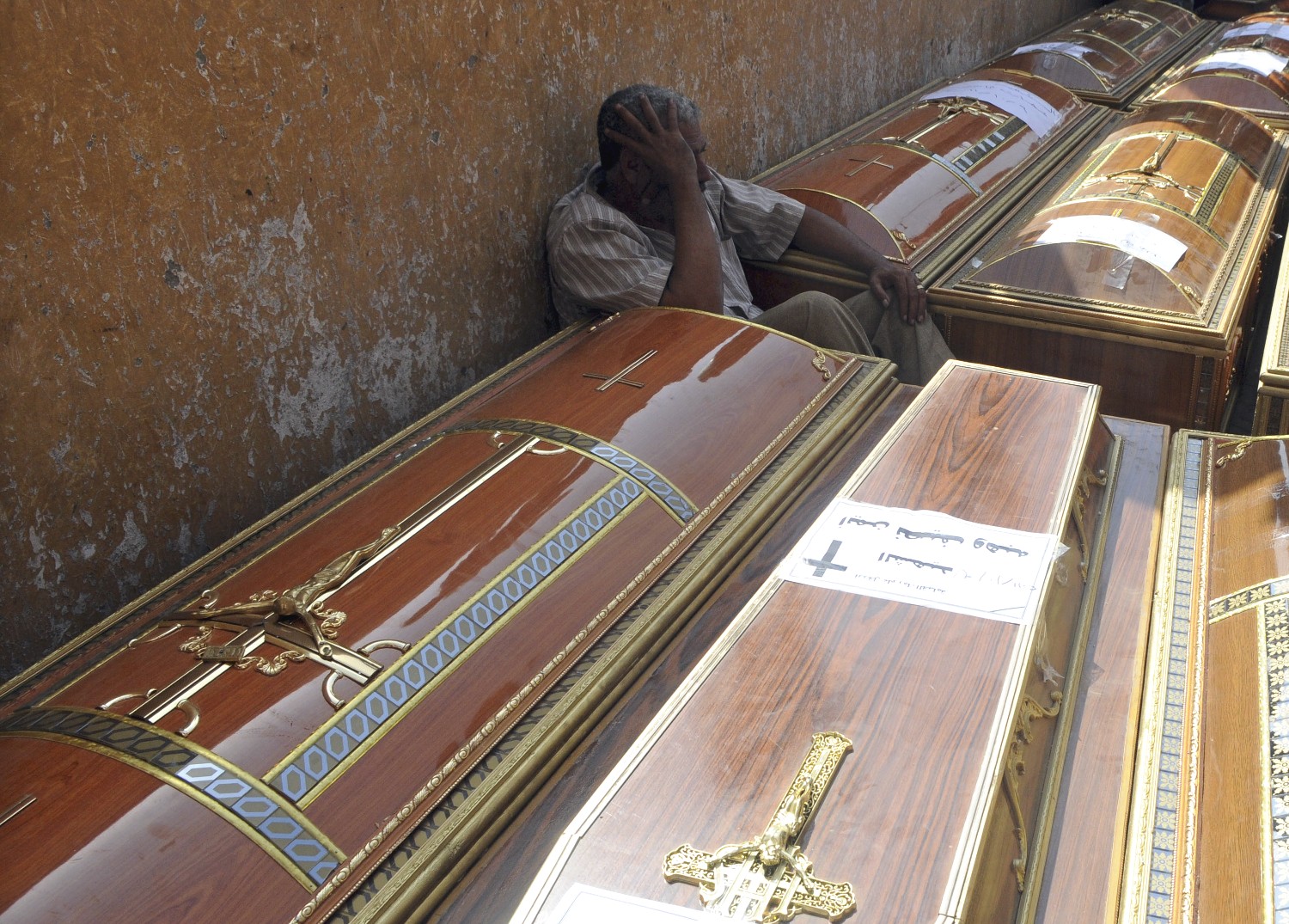 Man mourns next to one of many coffins outside of Coptic Hospital