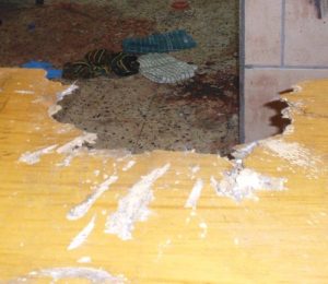 The bomb planted by Jack Teitel exploded on a solid oak table tearing a hole it it. Amiel's blood can be seen on the floor behind the table.